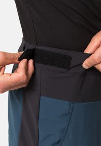 Ceinture réglable des pantalons bleus et noirs avec un système de fermeture à crochet et boucle. Gros plan montrant la texture et les détails de construction.