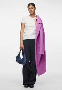 Lila Übergröße Mantel, weißes T-Shirt, gestreifte marineblaue Hose und eine blaue Handtasche mit Muster. Der Mantel hat einen Reverskragen und Taschen.