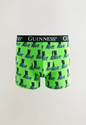 Kirkuvan vihreät boxershortsit, joissa toistuva kilpikonnakuosi, jossa kilpikonnat kantavat tuoppeja Guinnessia, ja musta vyötärönauha, jossa on valkoinen Guinness-logo.
