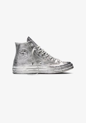 Sneaker metallizzata alta argento con lacci bianchi, suola testurizzata e toppa circolare alla caviglia, vista laterale.