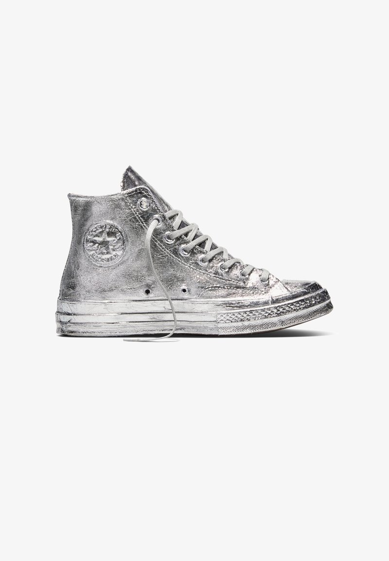 Sølvmetallic højt sneaker med hvide snørebånd, tekstureret sål og cirkulært mærke på anklen, vist fra siden.