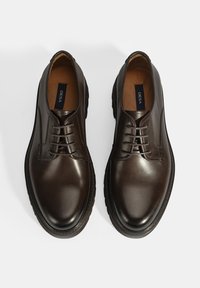 Chaussures en cuir marron avec une finition lisse, bout arrondi et design à lacets. Dotées d'une semelle durable et d'une doublure intérieure en beige. Étiquette de la marque visible.