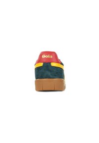 Zapatilla de ante verde con acentos rojos y amarillos. Presenta una suela de goma y un respaldo texturizado con el logo "Gola" en dorado. Diseño clásico.