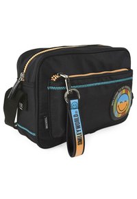 Bolsa de tela negra con dos compartimentos con cremallera, costuras azules y un parche de cara sonriente. Cuenta con una correa desmontable con el logo.