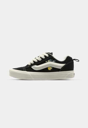Mustad musta kanvas sneaker valgete paelte ja külgtriibuga, lilleline tikand ja kollane aktsent, tekstureeritud kummitald, madal profiil.