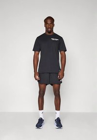 Crna sportska majica s kratkim rukavima s bijelim tekstom; uparena s crnim kratkim hlačama i tamnoplavim tenisicama za trčanje s bijelim detaljima.