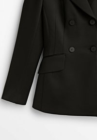 Veste noire à double boutonnage avec quatre boutons, poche à rabat et manches longues, montrée du milieu du torse jusqu'au poignet sur fond blanc.