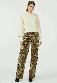 Pull beige à col montant, associé à un pantalon large taille haute à motif léopard. Des escarpins noirs complètent le look.
