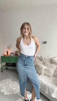 Τζιν φούστα με ψηλή σχισμή και ακατέργαστο τελείωμα, με ελαφρύ μπλε πλύσιμο. Συνδυασμένη με λευκό τοπ αμάνικο και μαύρα παπούτσια.