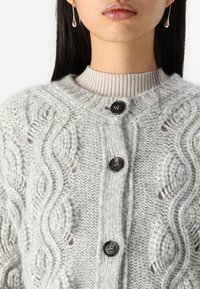 Cardigan tricotat gri deschis, cu un model cu cabluri, guler striat și trei butoane negre în față. Material moale, texturat.