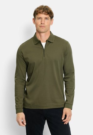 Dark green long-sleeve polo shirt with a half zipper, featuring a collared neck and a smooth, textured fabric. Styled with black corduroy pants.