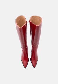 Par boots visokih, sjajnih crvenih kožnih čizama sšiljatim prstima i bež unutrašnjim oblogom, prikazanim odozgo na bijeloj pozadini.