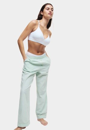 Bílý bralet a světle zelené pruhované kalhoty s bočními kapsami, které mají volný střih a elastický pas. Měkký bavlněný materiál.