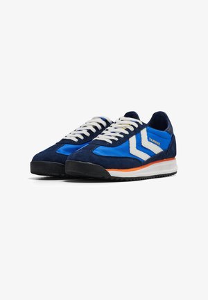 Paar blaue und marineblaue Sneaker mit weißen Schnürsenkeln, weißen Chevron-Streifen, orangefarbenen Akzenten und schwarzen Sohlen, nach links geneigt auf weißem Hintergrund.