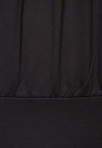 Svart tyg med en slät textur, som har samlad detaljer längs mitten och en platt midja i botten.