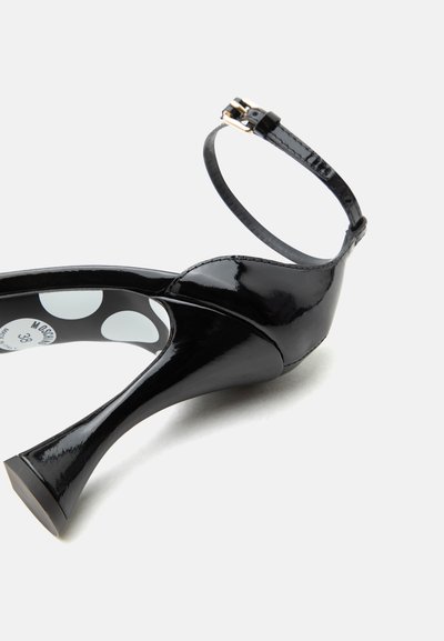 Μαύρο γυαλιστερό δερμάτινο ψηλοτάκουνο παπούτσι με λουράκι στον αστράγαλο και φουσκωτό τακούνι, που δείχνει την εσωτερική σόλα με πουά σχέδιο και ετικέτα μεγέθους.