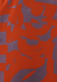 Tela roja con un patrón abstracto audaz en púrpura, con formas y texturas variadas. El diseño incorpora elementos gráficos en capas.