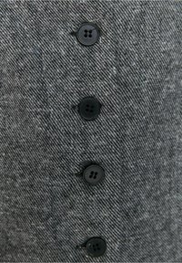 Gros plan sur un tissu texturé gris foncé avec quatre boutons noirs à quatre trous cousus en ligne verticale.