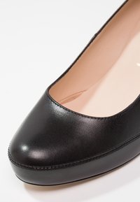 Ballerine plate en cuir noir avec un bout arrondi, un détail de couture visible le long du bord, et une doublure intérieure lisse.