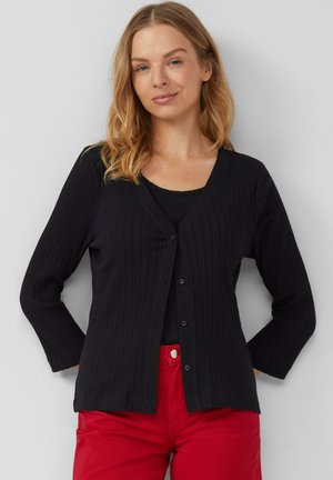 Schwarzer gerippter Cardigan mit V-Ausschnitt, langen Ärmeln und Knöpfen vorne, kombiniert mit einem schwarzen Oberteil und roten Hosen. Glatte Textur und enganliegendes Design.