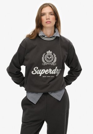 Dark gray sweatshirt with a crew neckline, white logo and detailing, layered over a blue and white striped collared shirt. Casual fit.