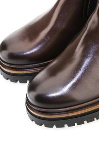 Gros plan de bottes en cuir brun foncé poli avec des semelles épaisses à crampons noires et une bordure brune superposée autour de la base.