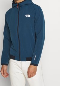 Granatowa bluza z kapturem na zamek, wykonana z miękkiego materiału. Posiada biały logotyp, elastyczne mankiety i sznurek do regulacji kaptura.