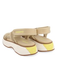 Sandalias de plataforma beige con parte superior de malla, correas ajustables y suela blanca acentuada con detalles amarillos. Presenta un logo en las correas.