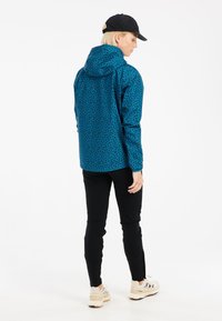 Mėlynos ir juodos raštuotos striukės su kapišonu, pasižyminčios laisvu siluetu. Dėvima su juodais kelnėmis ir šviesių spalvų sportbačiais.