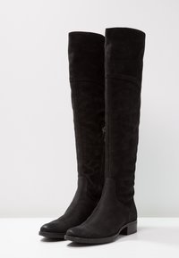 Botas negras por encima de la rodilla hechas de suave ante con un acabado liso, que cuentan con un cierre de cremallera en el lateral y un tacón bajo y cuadrados.