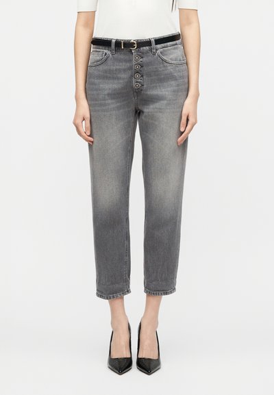 Γυναίκα που φοράει ξεβαμμένο γκρι τζιν με ψηλή μέση, διακοσμητικά κουμπιά και μαύρη ζώνη, συνδυασμένο με μαύρα παπούτσια με μυτερή μύτη.