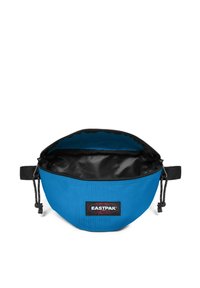 Borsa in tessuto blu con forma arrotondata, interno nero e chiusura a zip. Presenta una tracolla regolabile e un evidente patch con il logo Eastpak.