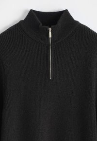 Pull en maille côtelée noire avec un col montant et une fermeture éclair demi zip argentée au centre devant.