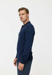 Pulover bleumarin cu guler plat și mâneci lungi, fabricat din țesătură tricotată, are manșete și tiv cu model ondulat. Potrivit pentru îmbrăcăminte casual.