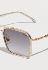 Gafas de sol con montura de metal dorado y lentes degradados en gris, con un diseño cuadrado, acentos claros y detalle grabado "CARRERA UV PROTECT".