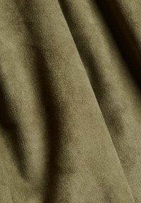 Olivi vihreä mokkafarba, jossa on pehmeä, teksturoitu pinta ja hienovarainen kiilto, sisältäen sileitä taitoksia ja poimuja. Korkealaatuinen ja kestävä materiaali.