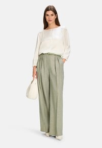 White satin blouse with gathered sleeves, green textured high-waisted trousers, light green belt, and a light beige handbag.