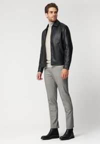 Czarna skórzana kurtka z kołnierzem, noszona na jasnym beżowym golfie. Szare spodnie w wzór hounds-tooth oraz czarne botki do kostek uzupełniają strój.