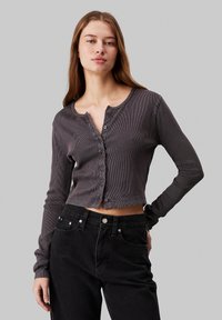 Tummanharmaa ribbikerros pitkällä hihaisella cropped-neuleella, jossa on pyöreä pääntie, etupainike suljenta ja istuvat hihat, yhdistettynä korkeavyötäröisiin mustiin farkkuihin.