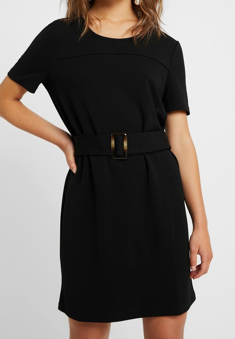 Czarna sukienka z krótkimi rękawami, okrągłym dekoltem i dopasowanym stanem. Posiada szeroki pasek z prostokątną klamrą. Gładki, strukturalny materiał.