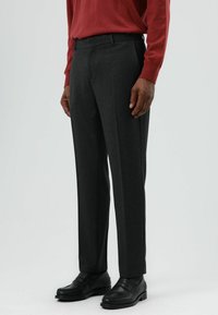 Donkergrijze, op maat gemaakte broek van gladde stof, met een rechte pijp en riemlussen, gecombineerd met zwarte schoenen.