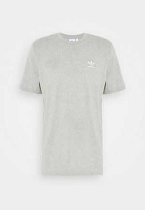 Camiseta gris con logo, pantalones jogger en negro y gris con detalles de acento, gorra blanca con logo y zapatillas deportivas negras.
