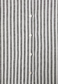 Camicia a righe con bottoni, realizzata in tessuto leggero. Presenta righe verticali bianche e nere, con cinque bottoni circolari bianchi.