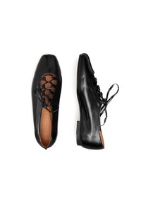 Scarpe in pelle nera con punta affusolata, caratterizzate da un design a laccio incrociato e suola piatta. Texture liscia con una finitura lucida.