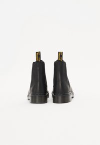 Zwarte leren chelsea boots met elastische zijpanelen, een gestikte zool en gele lussen met de tekst "Bouncing" op de achterkant.