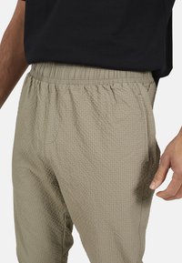 Jasne beżowe spodnie teksturowane z elastycznym pasem, z wzorem w kratkę i bocznymi kieszeniami. Połączone z czarną koszulką.