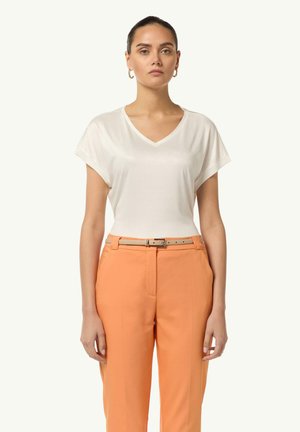 V-neck, short sleeve white t-shirt made of soft fabric, paired with high-waisted orange trousers held by a light tan belt with a silver buckle.