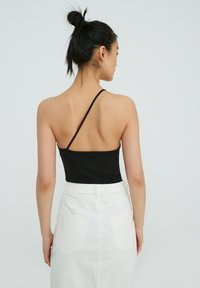 Zwart geribbelde bodysuit met een enkele schouderband, gecombineerd met een wit high-waisted denim rokje met achterzakken en een gladde textuur.