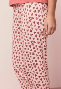 Růžové pyžamové kalhoty s celoplošným vzorem různých červených srdcí. Měkký materiál s volným střihem a elastickým pasem.