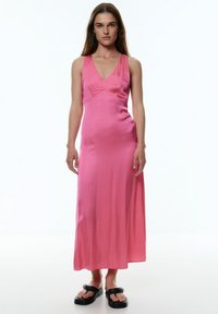 Rosa satin Maxi-Kleid mit V-Ausschnitt, tailliertem Oberteil und fließendem Rock. Das Model trägt schwarze Plateausandalen. Einfaches und elegantes Design.